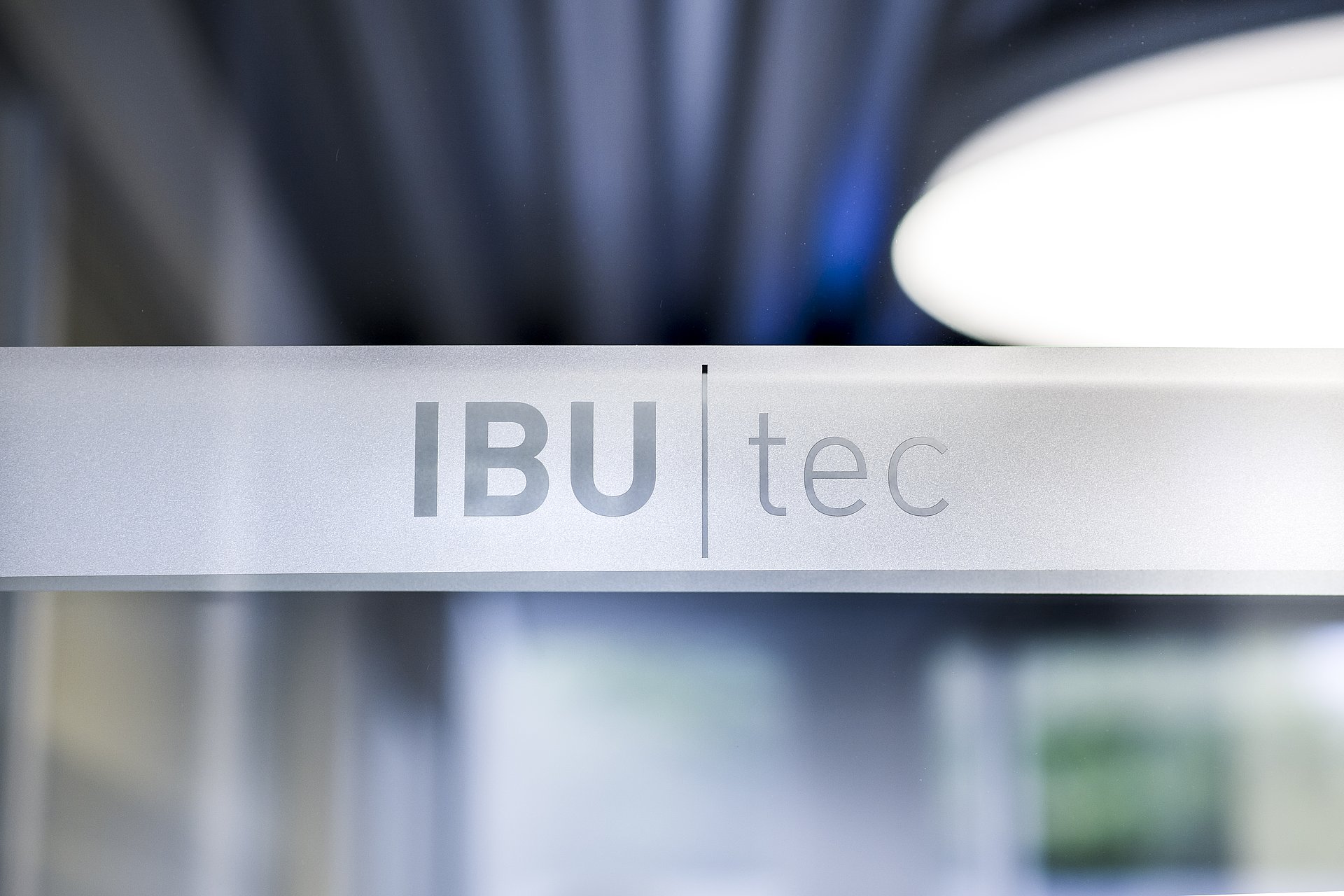 Logo IBU-tec avec des lumières floues artistiques en arrière-plan: bleu, gris et blanc